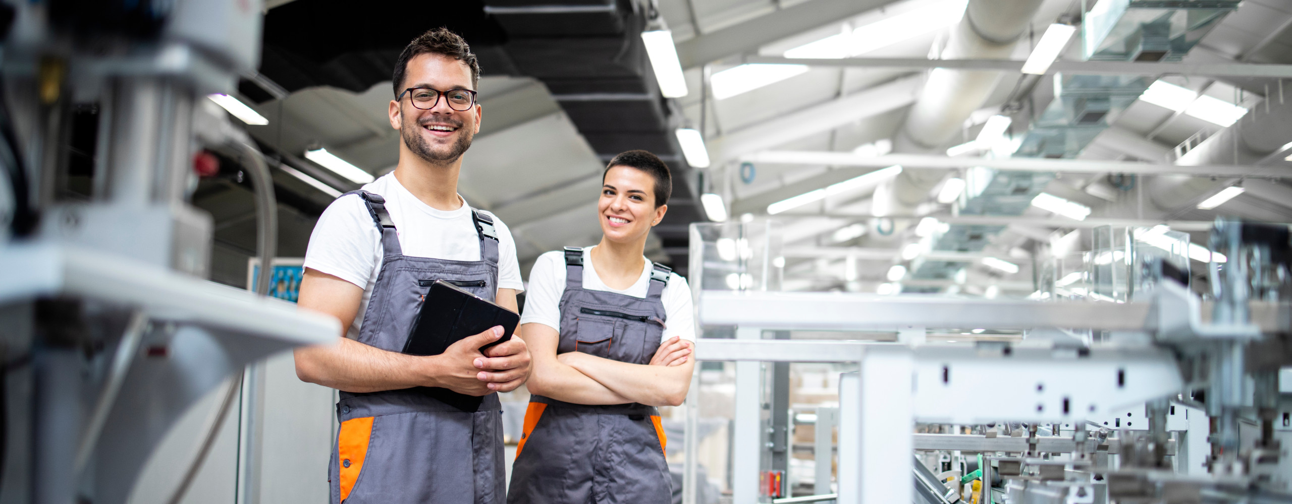 Ein Mann und eine Frau stehen vor einer industriellen Packmaschine und kontrollieren den Prozess.