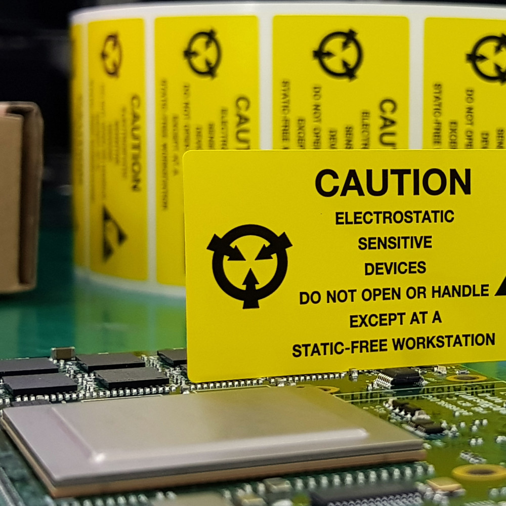 Eine elektronische Platine liegt auf einem ESD-Arbeitstisch. Ein gelbes Schild weist auf die Risiken von elektrostatischer Entladung hin.