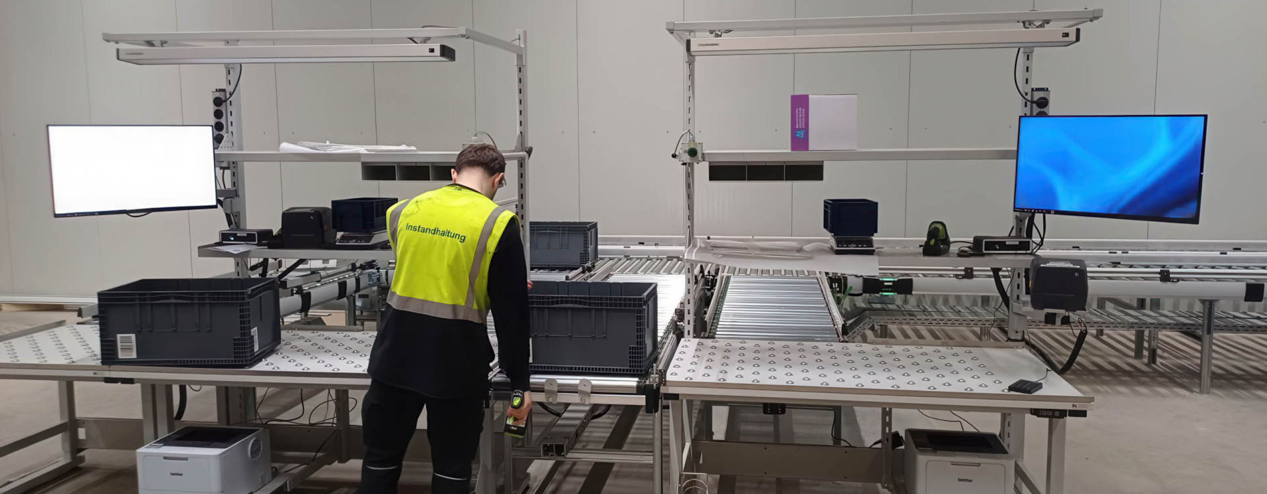 Ein Mann mit Warnweste befindet sich in einer Produktionshalle und arbeitet an einer Logistik-Packstation.