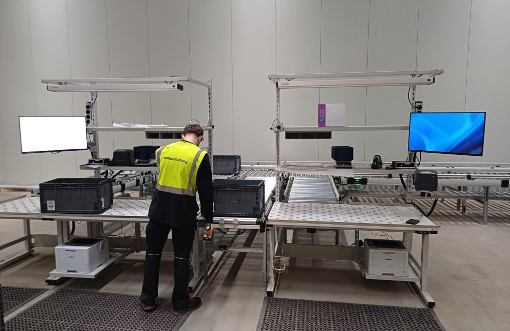 Ein Mann mit Warnweste befindet sich in einer Produktionshalle und arbeitet an einer Logistik-Packstation.