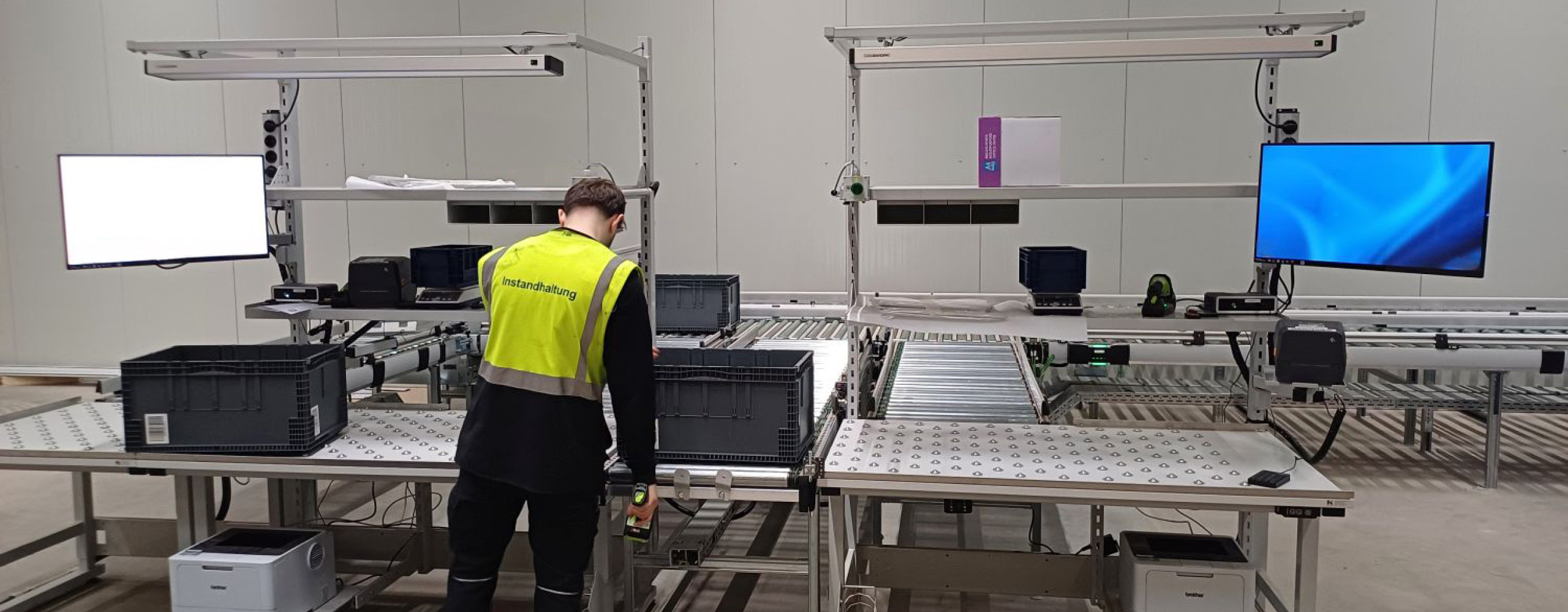 Ein Mann mit Warnweste befindet sich in einer Produktionshalle und arbeitet an einer Logistik-Packstation.