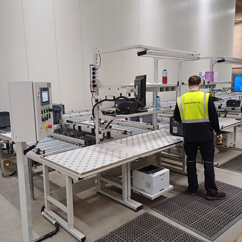 Ein Mann mit Warnweste befindet sich in einer Produktionshalle und arbeitet an einer Logistik-Packstation.